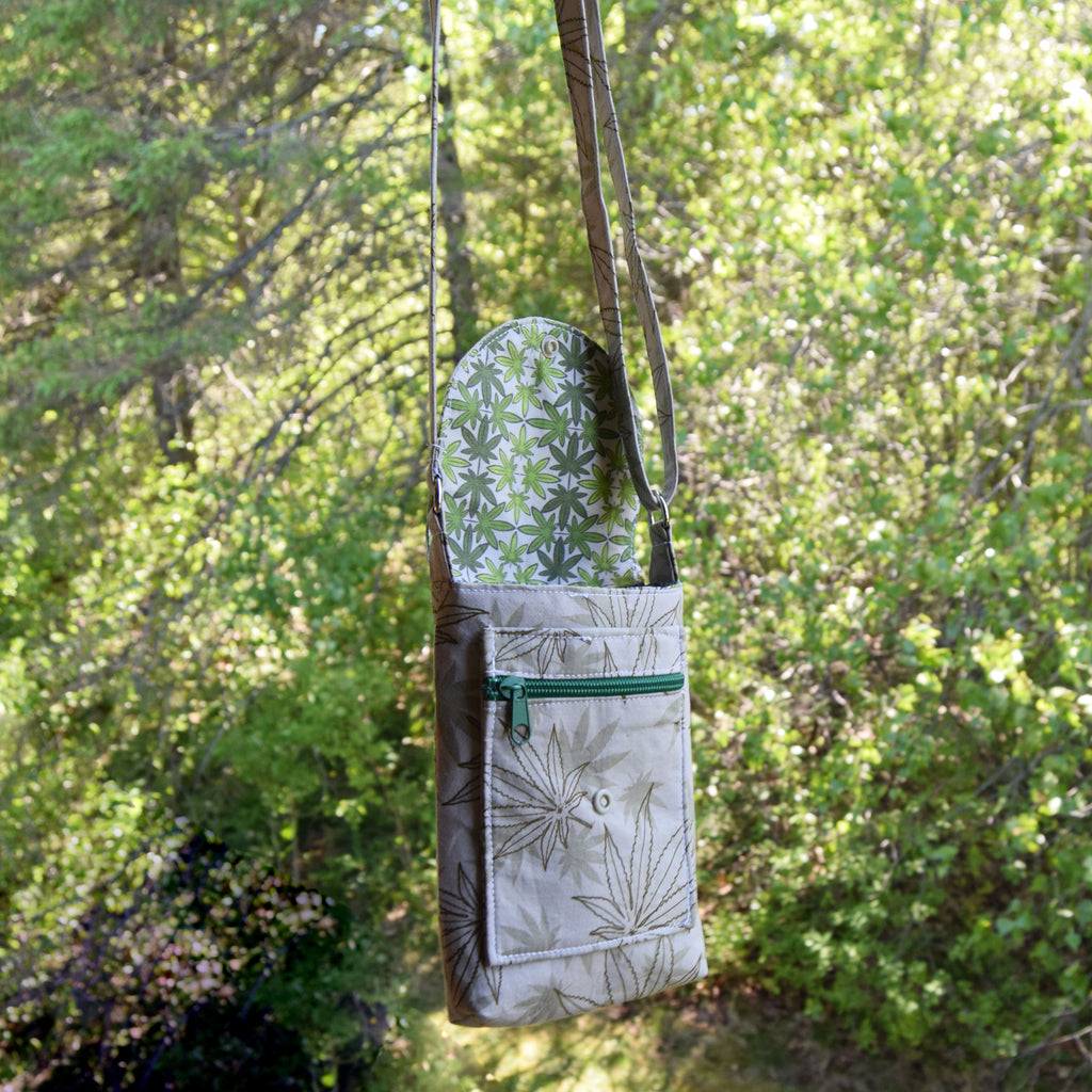 Green and white patterned bag hanging from a tree branch with a forest background