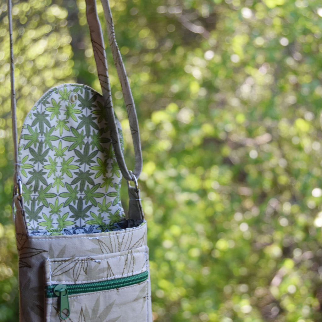 Tote bag with green weed leaf pattern hanging on a tree branch against a blurred green forest background